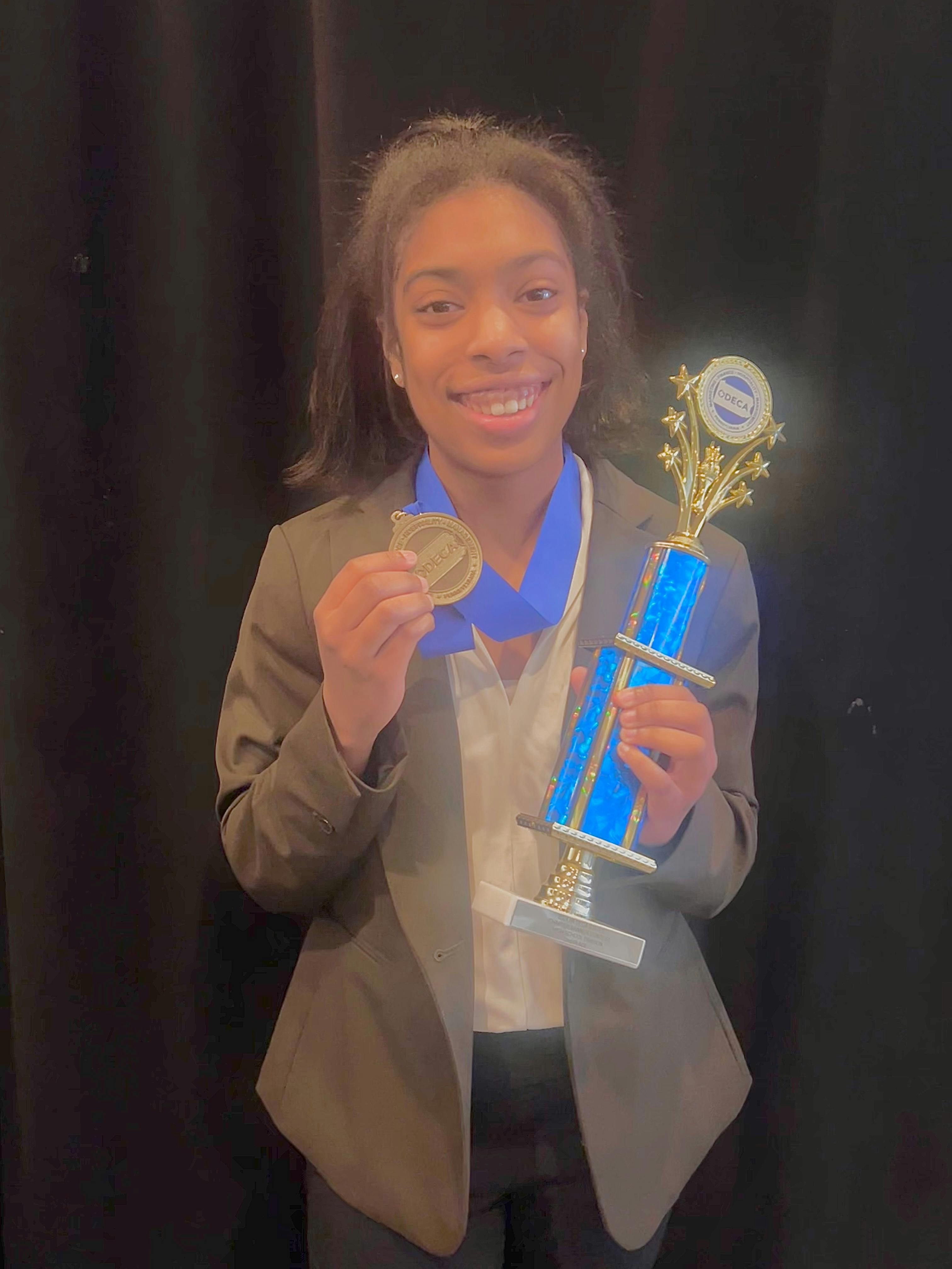 Young woman holds trophy that says DECA on it. She is also wearing a medal around her neck.