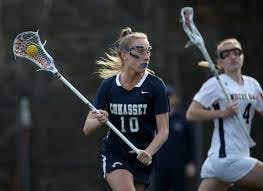 An action shot of Zennette playing lacrosse. She is holding the lacrosse stick with the ball in the scoop the stick. Her opponent is standing behind her.