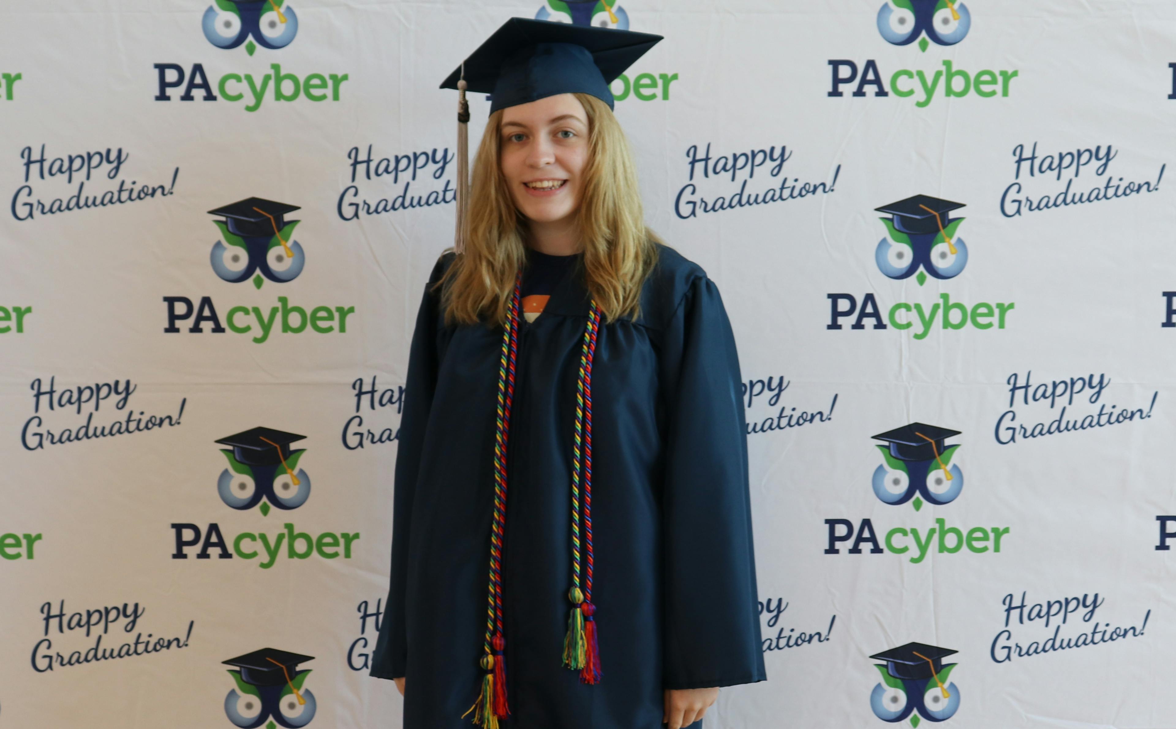 Riley wears a blue cap and gown for graduation, along with red and green cords representing clubs she belonged to.