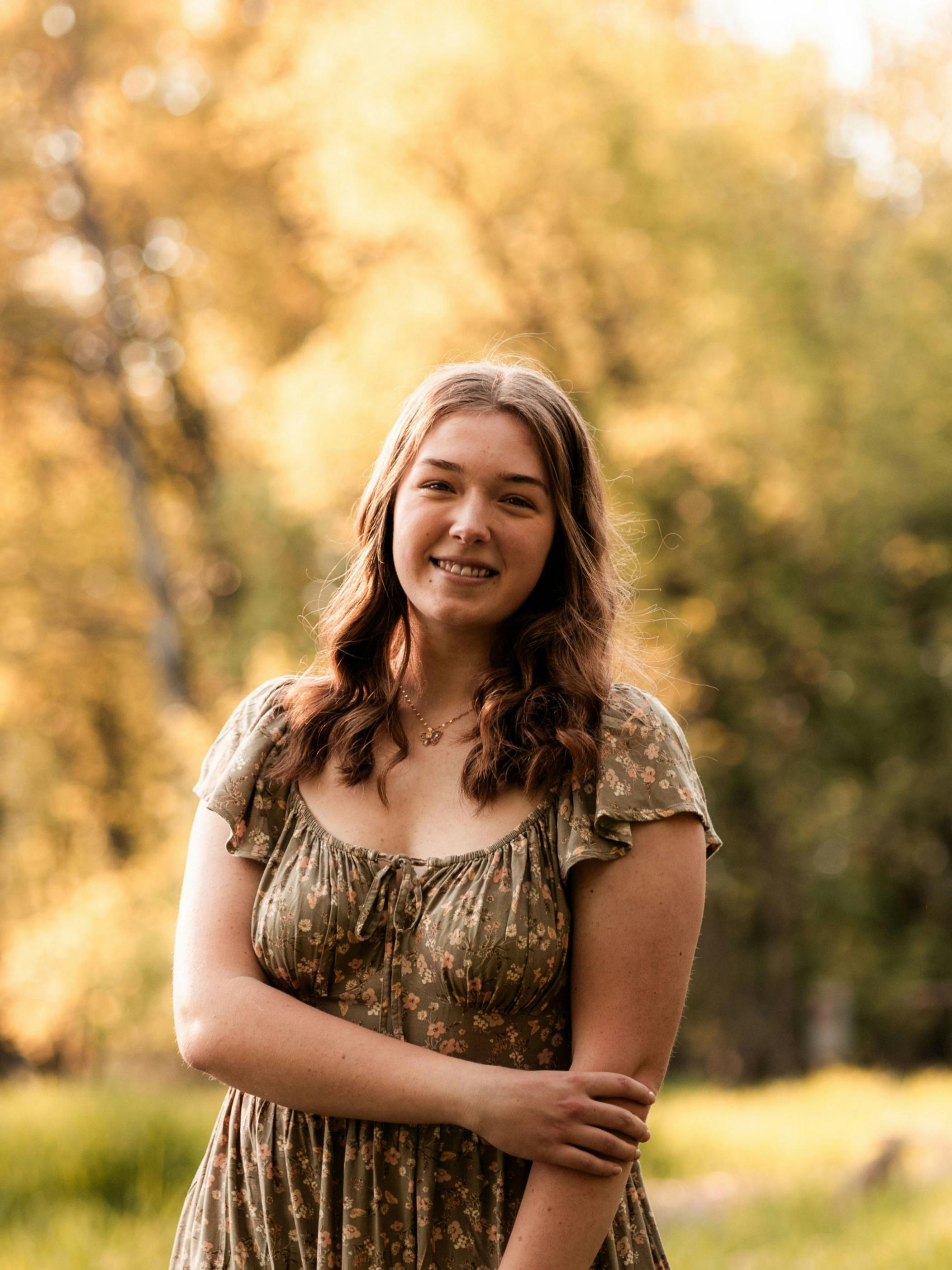 Abigail wearing a dress, standing in the middle of the frame, with yellow tree's in the background