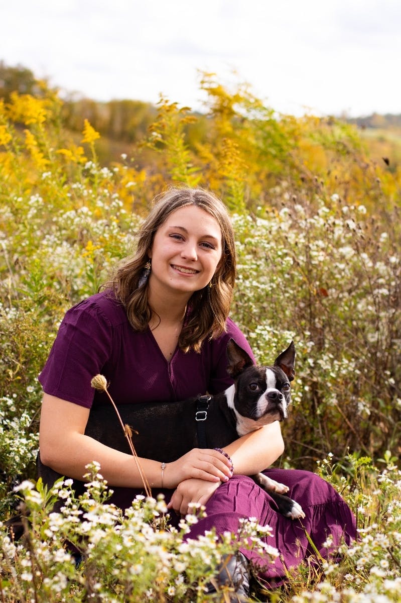 Young woman sits in a field while holding a Boston Terrier.