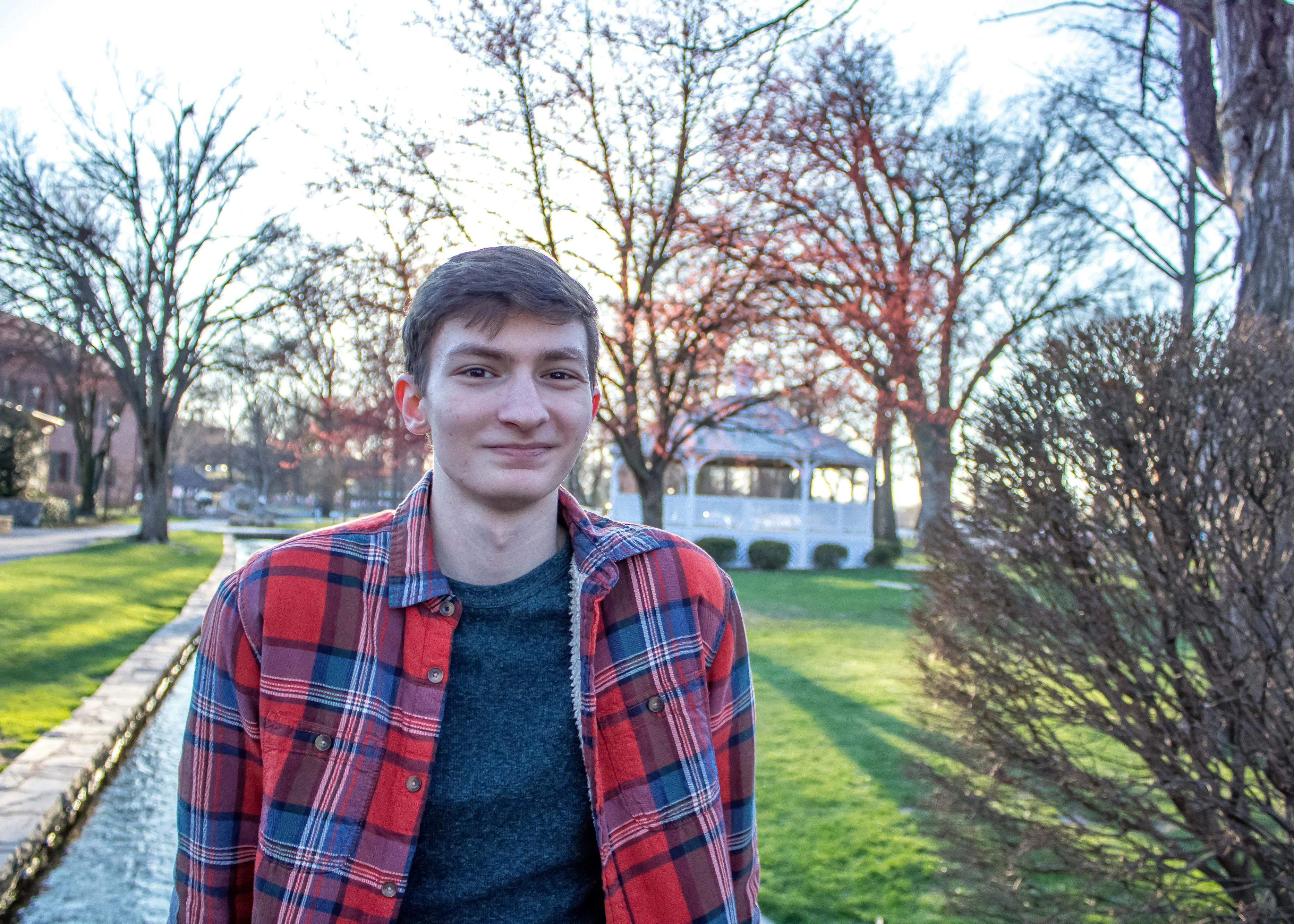 Donovan smiling at the camera wearing a plaid shirt, with a park in the background