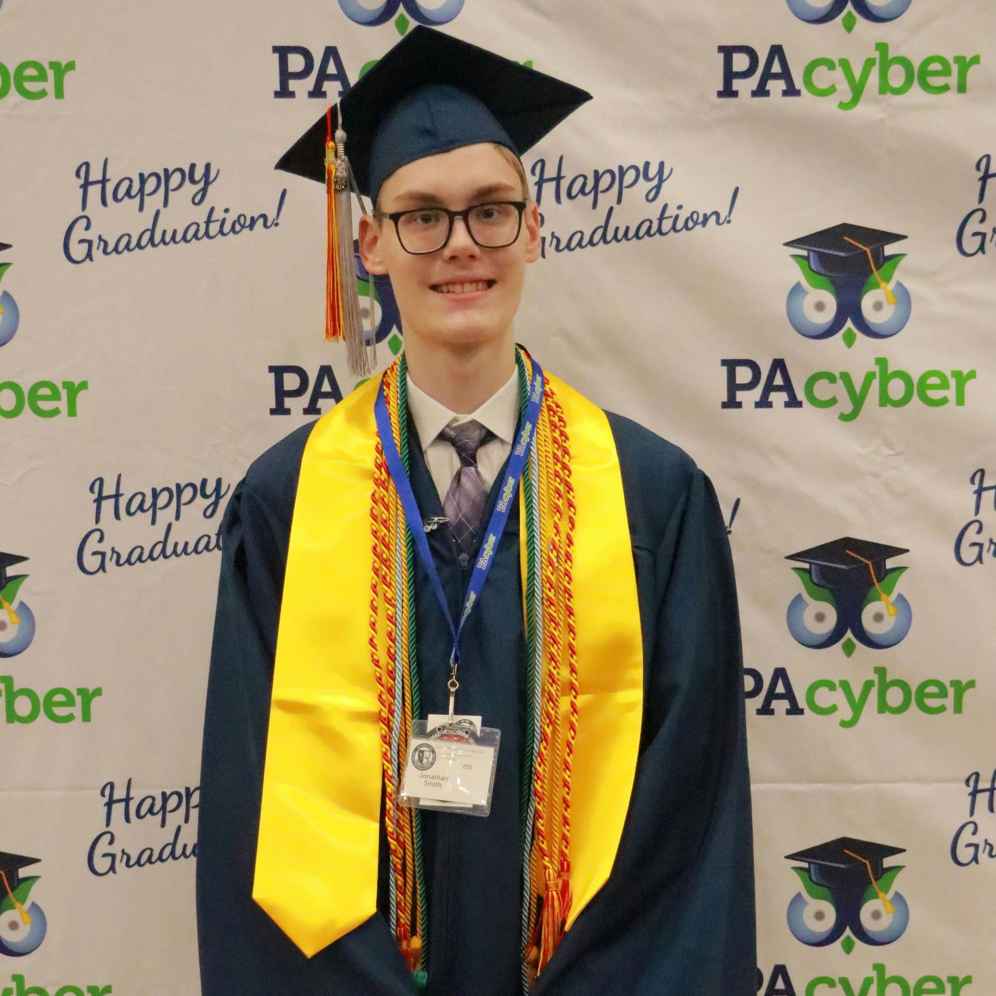 A male graduate wearing a navy cap and down and decorated with many-colored cords and stoles..